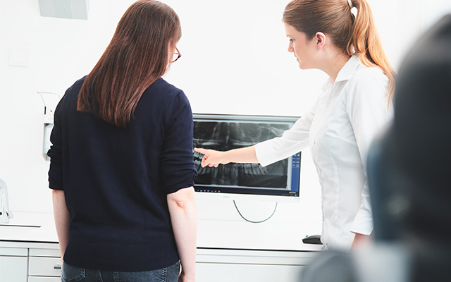 Zahnärztin zeigt einer Patientin Röntgenaufnahmen am Monitor 