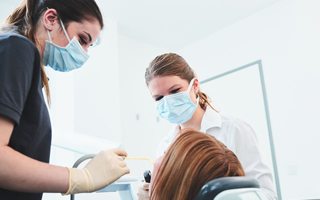 Patientin liegt auf Behandlungsstuhl und wird von Zahnärztin und Assistentin behandelt