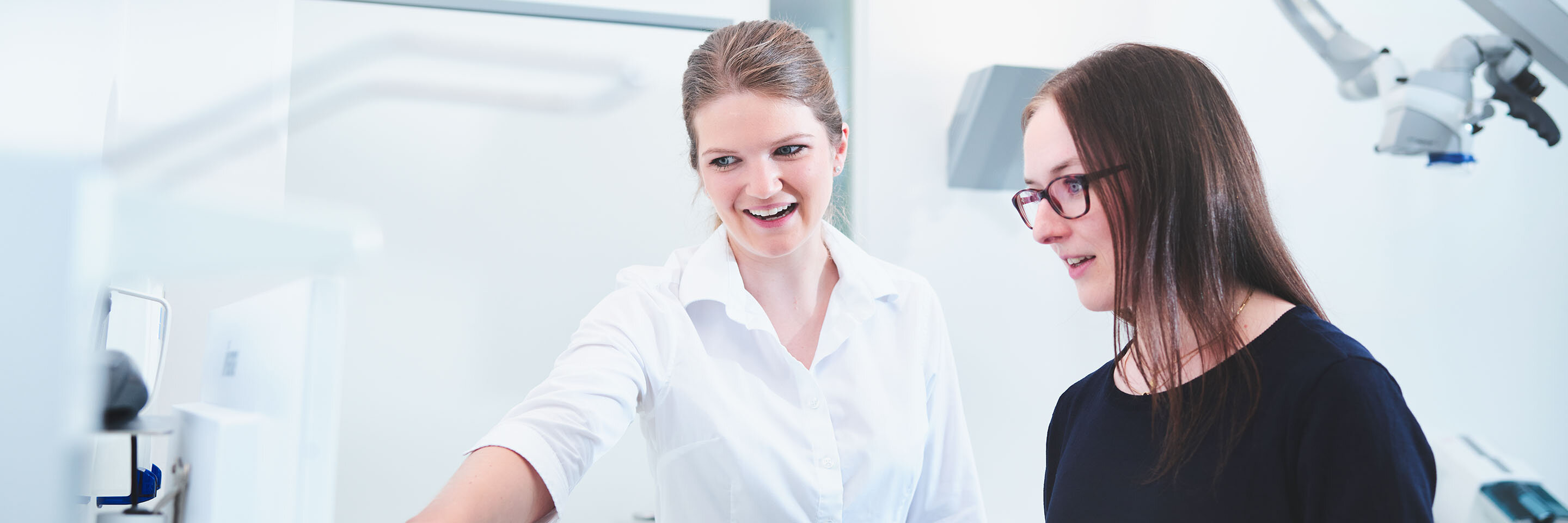 Eine Zahnärztin zeigt einer jungen braunhaarigen Patientin ihr Röntgenbild.