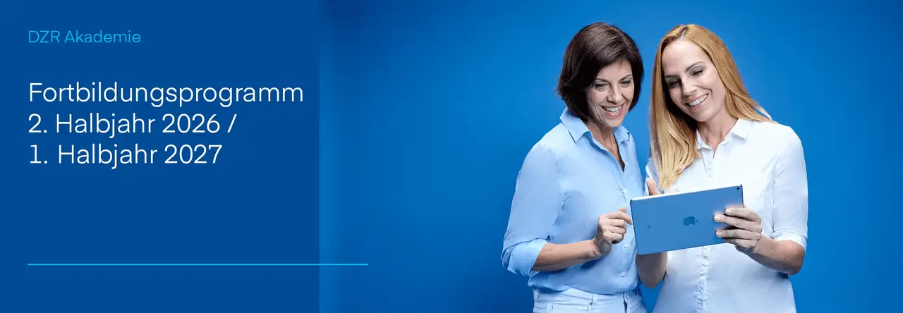 Zwei lächelnde Frauen schauen gemeinsam auf ein Tablet vor blauem Hintergrund.
