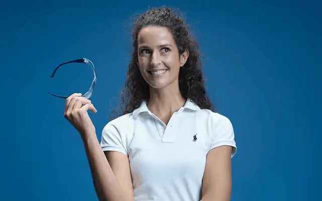Lächelnde Zahnärztin in weißem Polo-Shirt hält eine Brille in der Hand.
