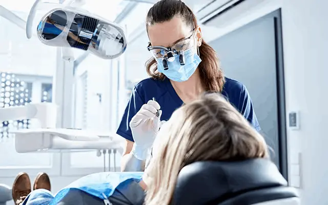 Zahnärztin mit Lupenbrille behandelt eine Patientin im Behandlungsstuhl.
