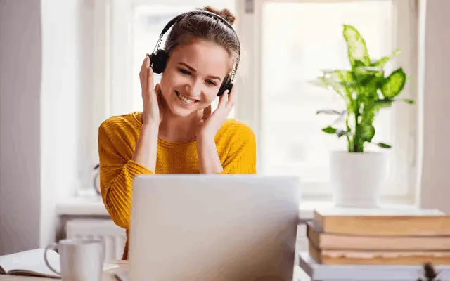 Junge Frau mit Kopfhörern lächelt beim Online-Lernen vor ihrem Laptop.