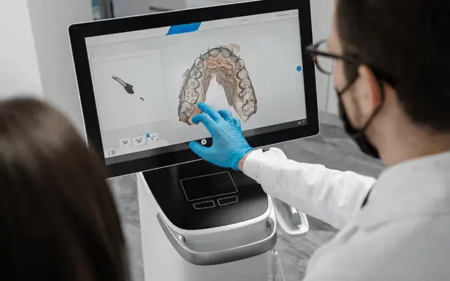 Zahnarzt zeigt Patientin ein 3D-Zahnmodell auf einem digitalen Touchscreen.