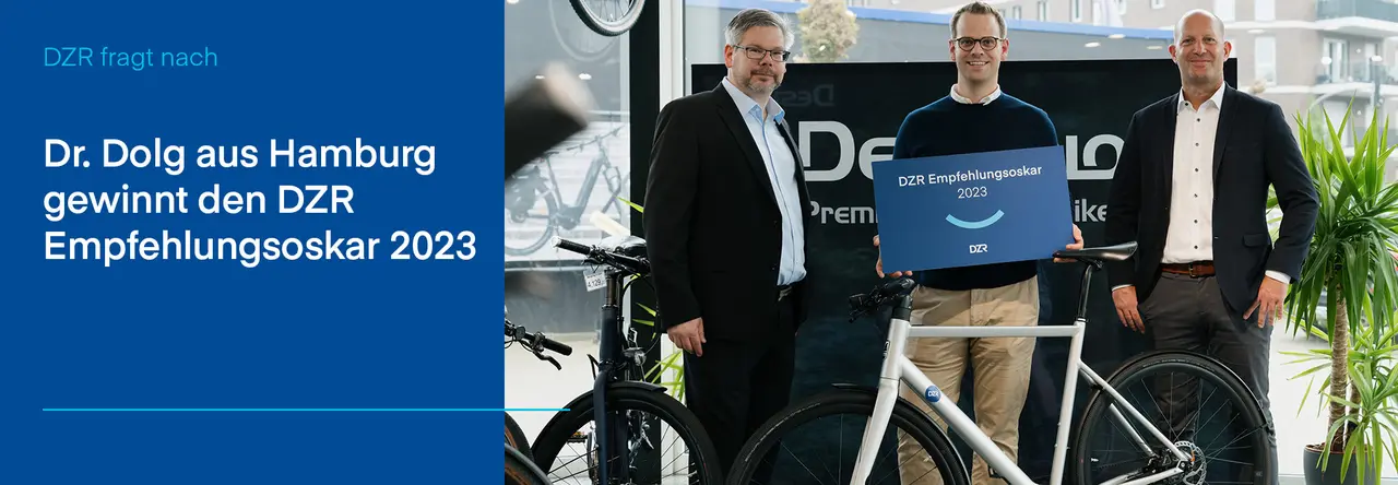 Zweigeteiltes Bild: Links blauer Hintergrund mit weißer Schrift "Dr. Dolg aus Hamburg gewinnt den DZR Empfehlungsoskar 2023", rechts Bild mit drei Personen, links Axel Engelhardt, in der Mitte Dr. Alexander Dolg, rechts Alexander Herz, davor ein E-Bike. Alle lächeln in die Kamera, Dr. Dolg hält eine Tafel mit "DZR Empfehlungsoskar 2023" in der Hand.